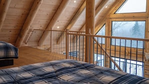 Una habitación con techo alto de madera, una cama, una ventana y una escalera.