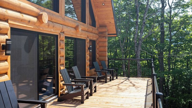 Una cabaña de troncos con terraza, mobiliario exterior y ventanas amplias.