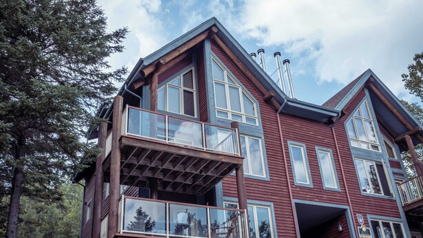 A multi-story wooden building with large windows and balconies, surrounded by trees.