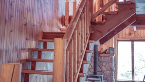 A wooden interior with a staircase, checkered sofa, and a stone fireplace.