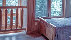 A wooden cabin with a loft bed, large windows, and a balcony.