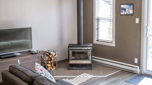 Ein Wohnzimmer mit Fernseher, einer Couch, einem Kamin und einem Fenster mit Jalousien.