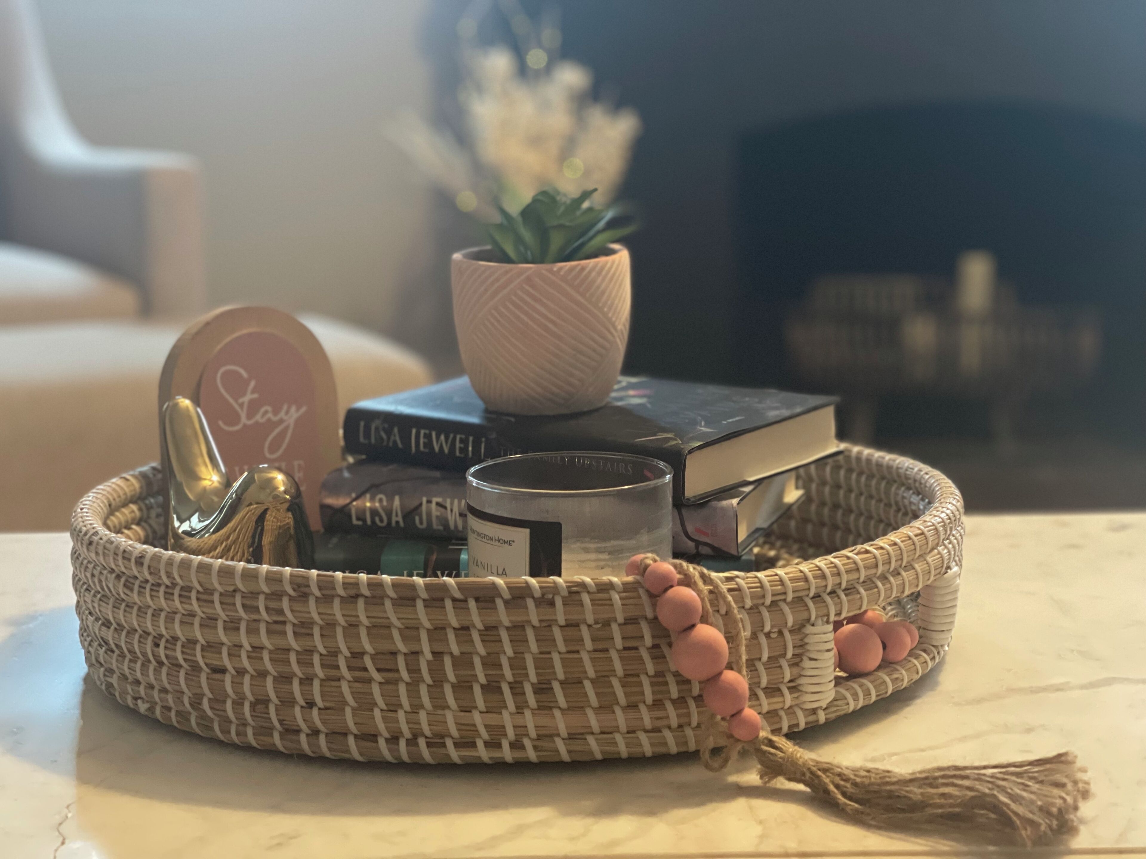 A woven basket containing books, a candle, and decorative items on a table.