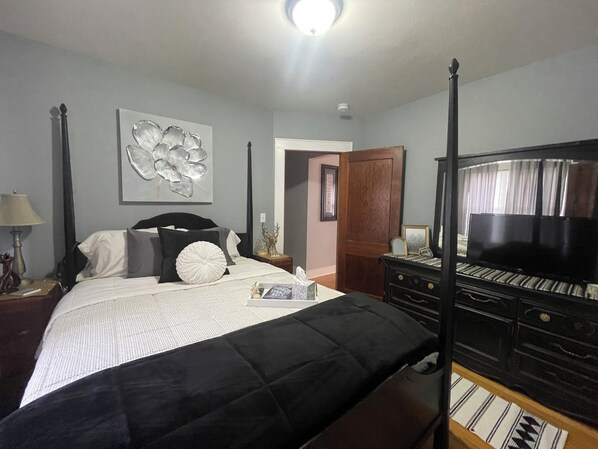 Un dormitorio con cama, televisor, piano y puerta que da a otra habitación.