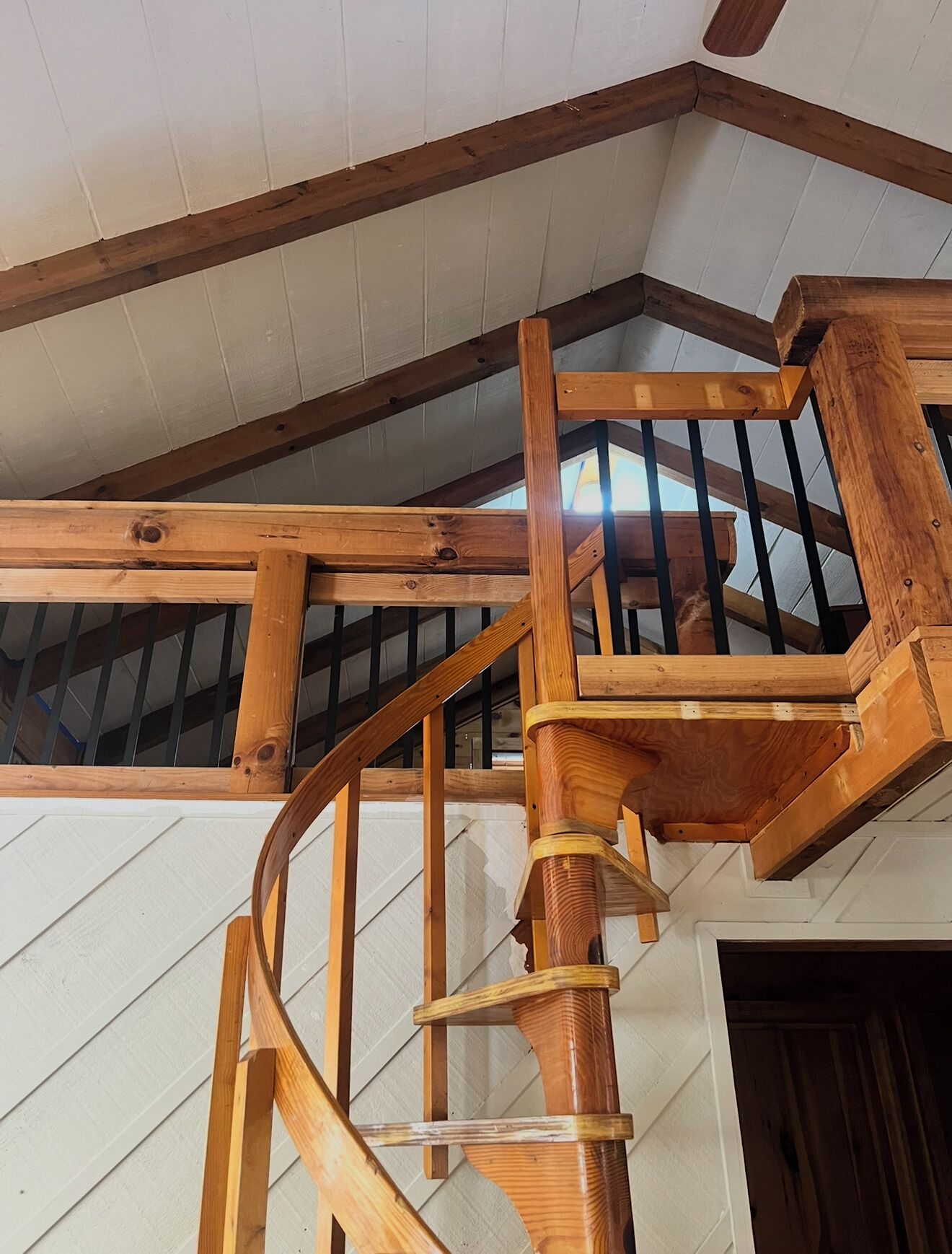 A wooden spiral staircase with a metal railing, leading to an upper floor with a sloped ceiling.