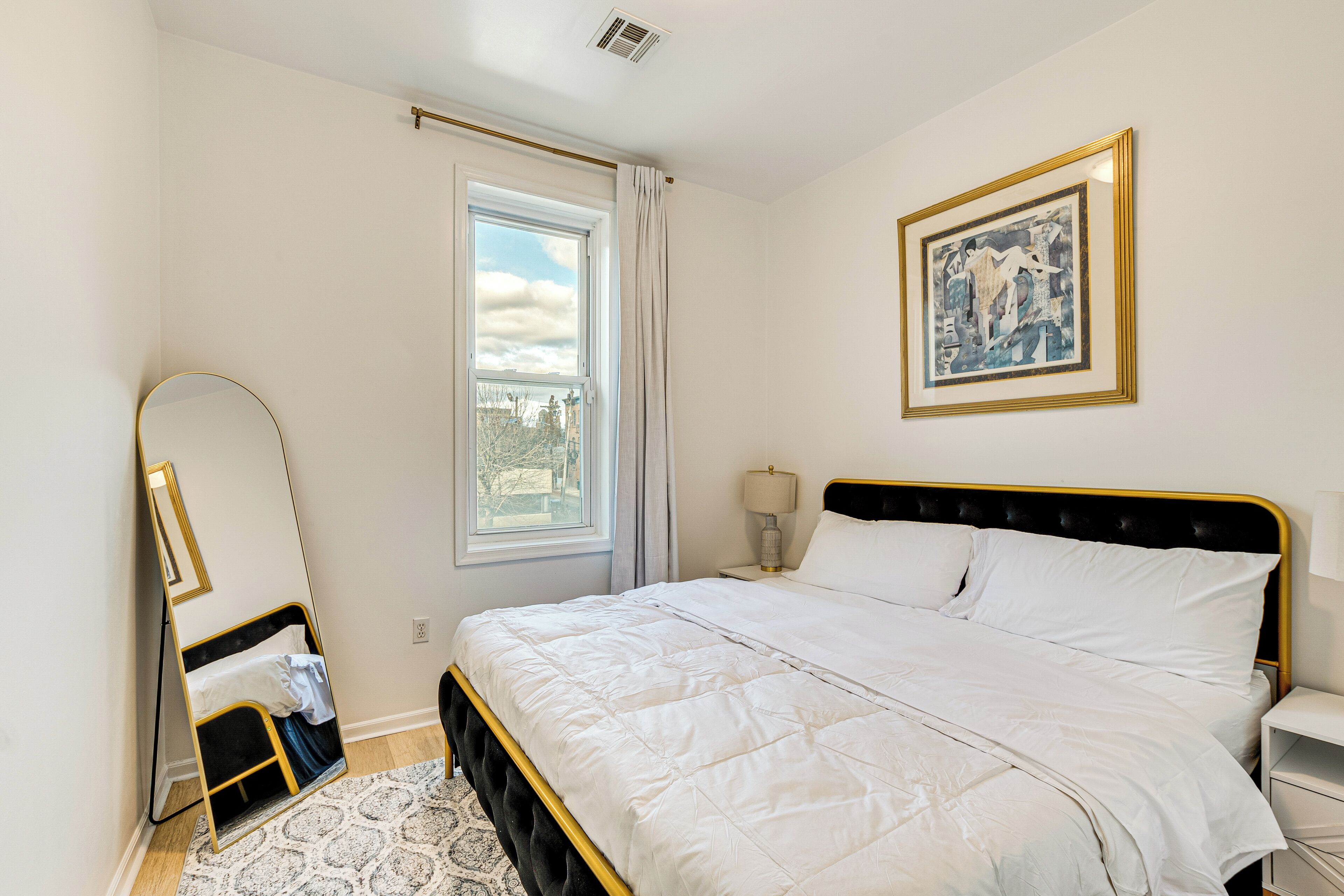 Una camera da letto ordinata con un letto grande, un comodino, uno specchio e una finestra con tende.