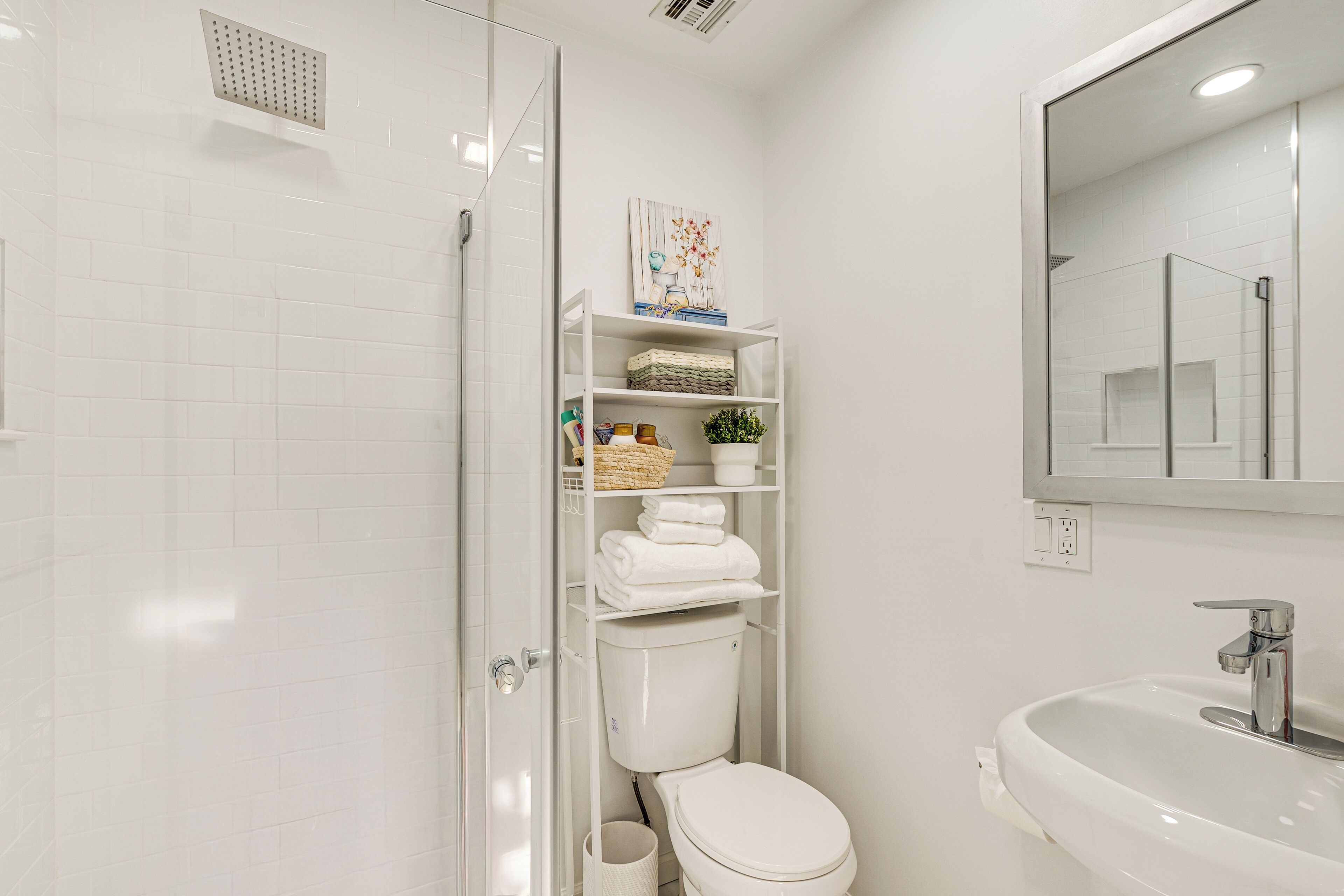 A modern bathroom with a glass shower enclosure, a white toilet, and a sink with a mirror above it.