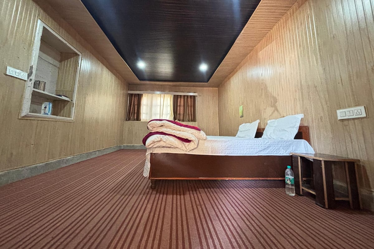 A hotel room with a wooden floor, a bed with white linens, a wooden headboard, and a small wooden table.
