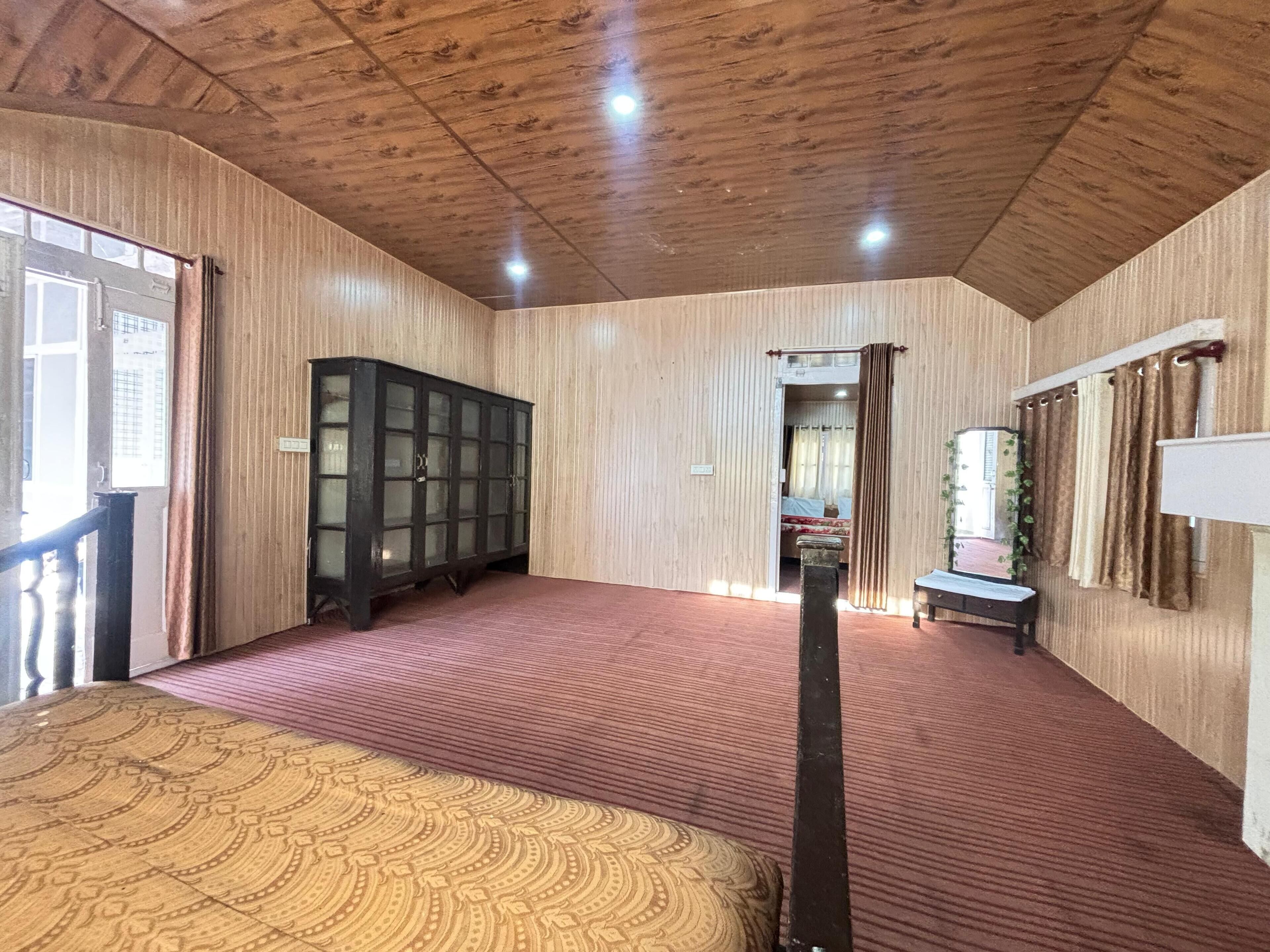 Een kamer met een houten plafond, een groot kast, een bed met beddengoed met een patroon en een bank.