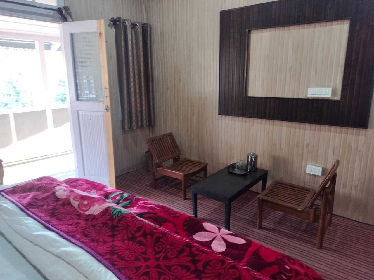A room with a bed, two wooden chairs, a small table, and a mirror on the wall.