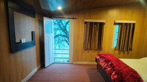 Una habitación con cama, ventana con cortinas, puerta que da al exterior y una pequeña estantería con objetos en la pared.