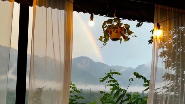 Una habitación con vistas a montañas y un arcoíris, con cortinas translúcidas.