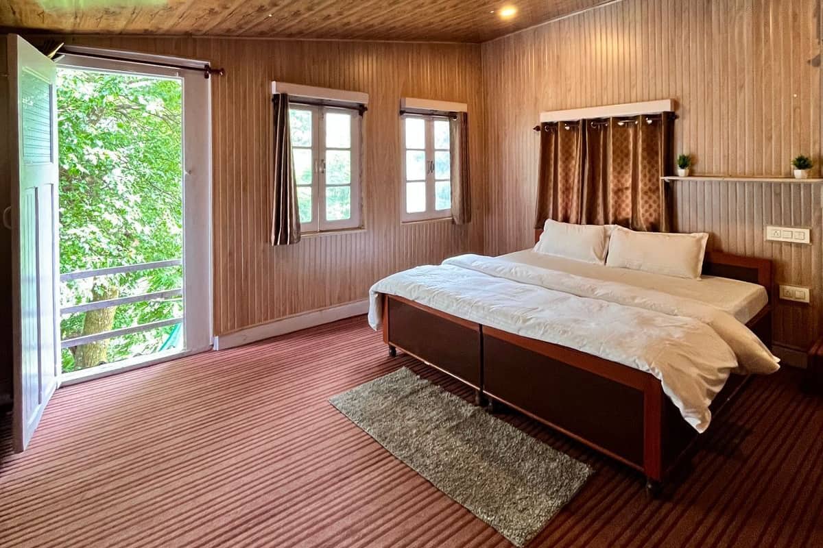 A bedroom with a wooden ceiling, a large bed, a window, and a view of greenery outside.