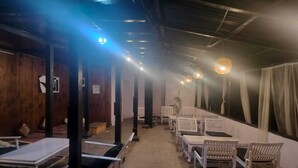 Una habitación con paredes y techo de madera, camas blancas y una mesa larga con sillas.