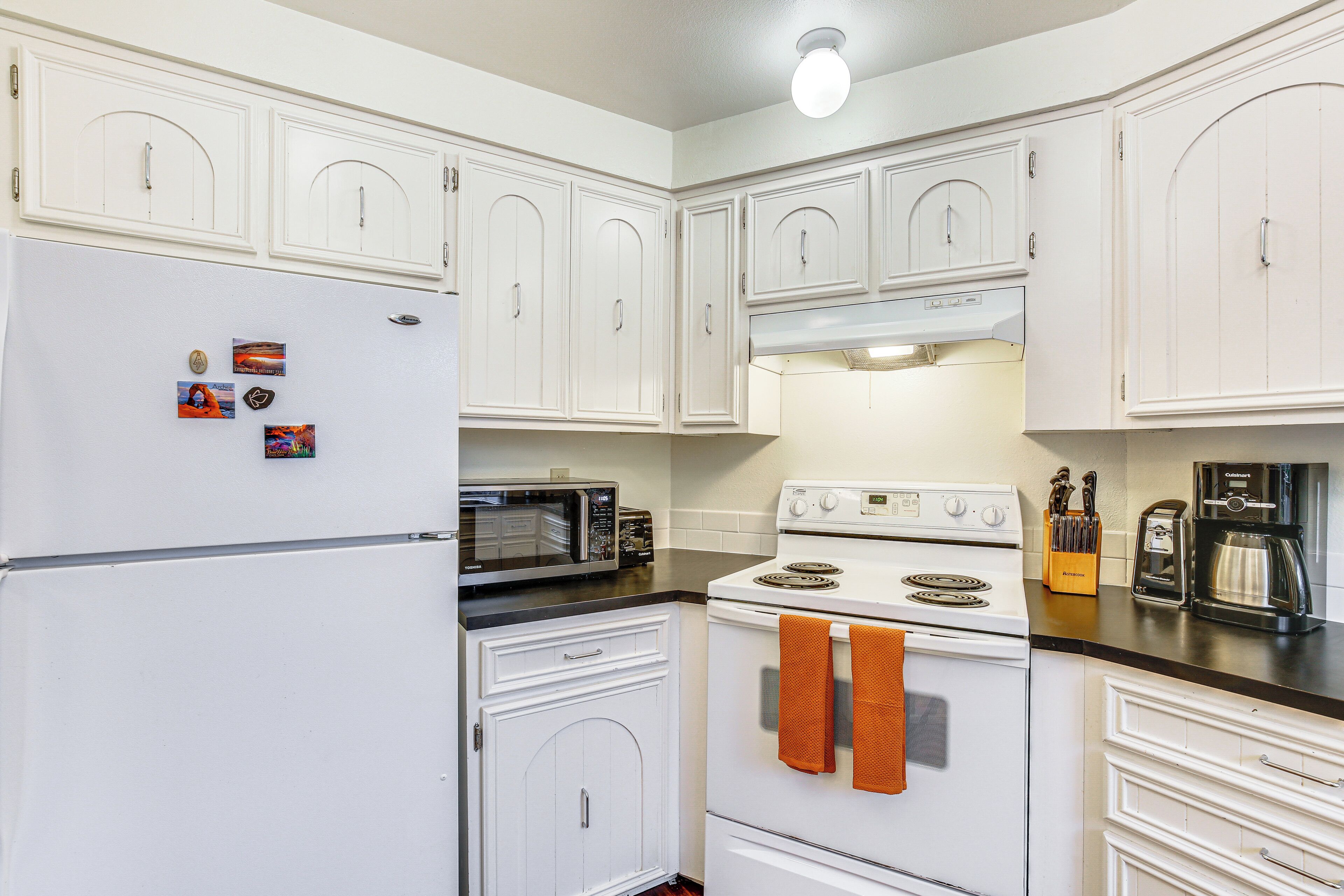 A kitchen with white cabinets, a refrigerator, a microwave, a stove, and a coffee maker.