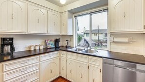 A kitchen with white cabinetry, a stainless steel dishwasher, and a window with a view of a house.