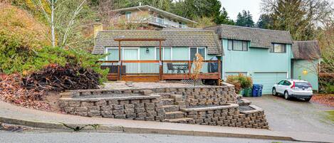 A two-story house with a front porch, a stone retaining wall, and a car parked in the driveway.