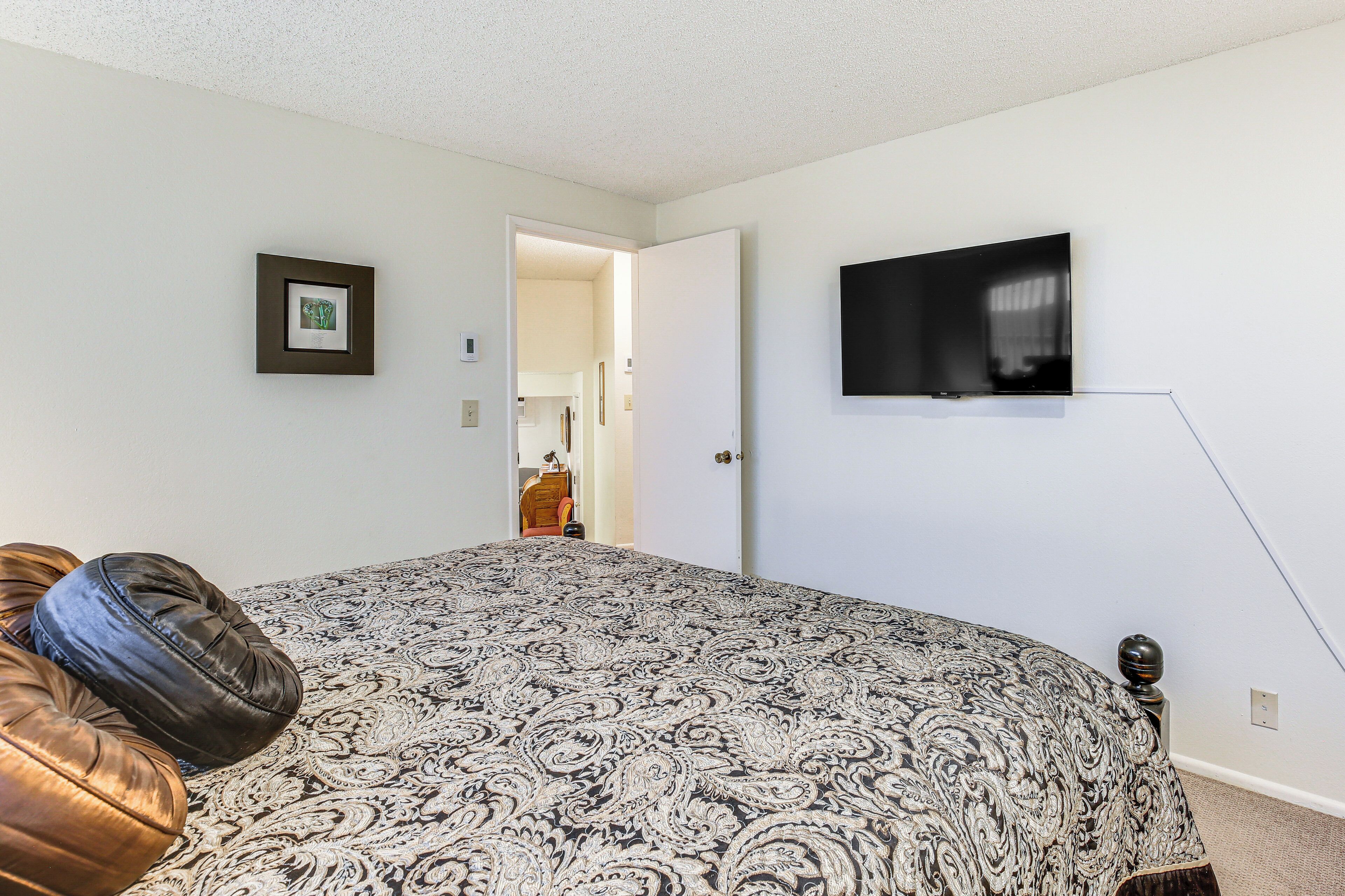 Een slaapkamer met een bed met een gestreept sprei, een aan de muur bevestigde televisie en een deur die naar een andere kamer leidt.