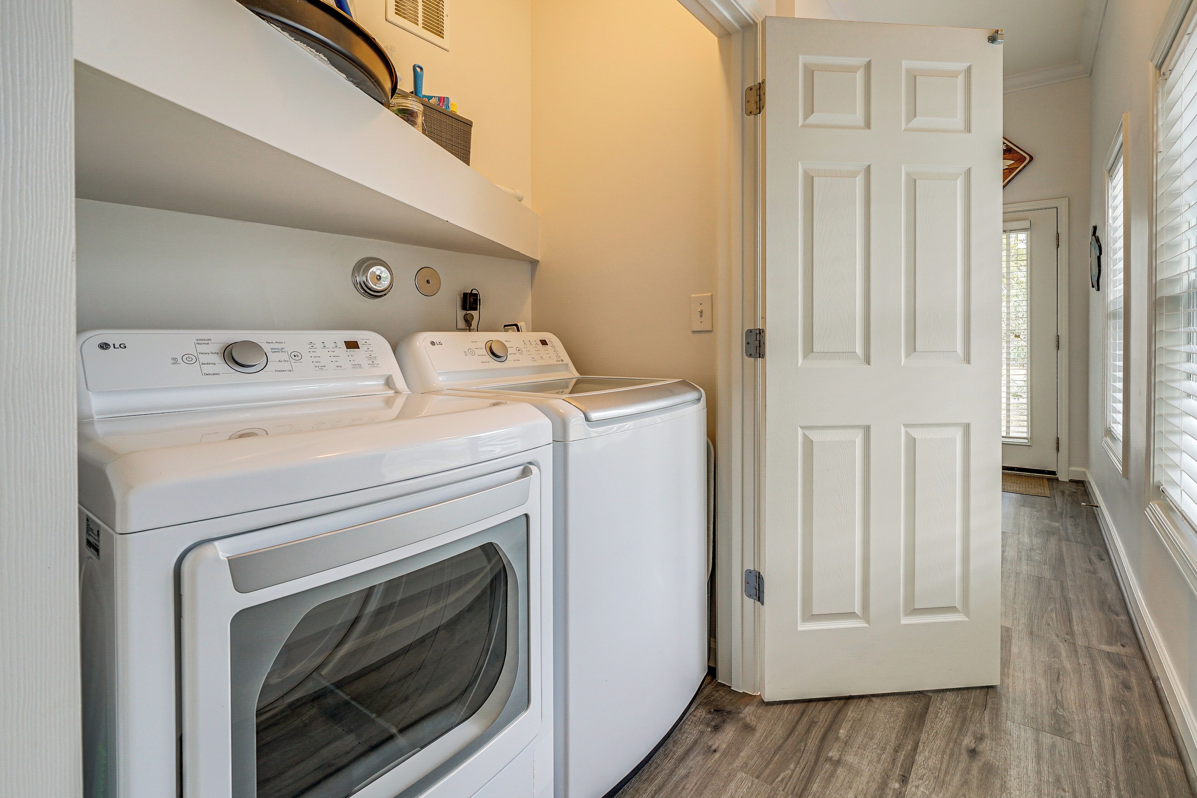 A laundry area with two white washing machines and a dryer, a white door, and a wooden floor.