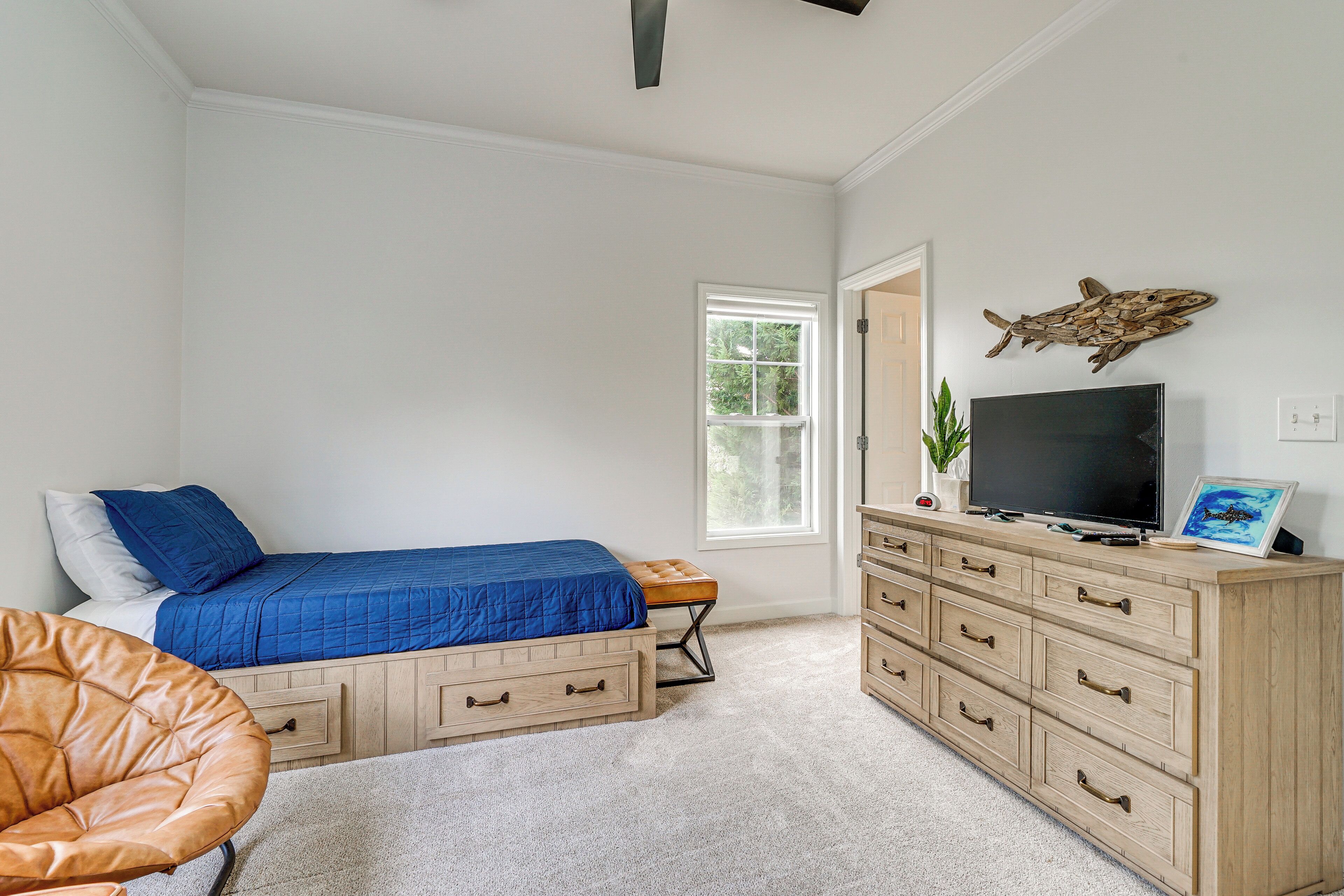 A bedroom with a bed, dresser, TV, and a fish wall art piece.