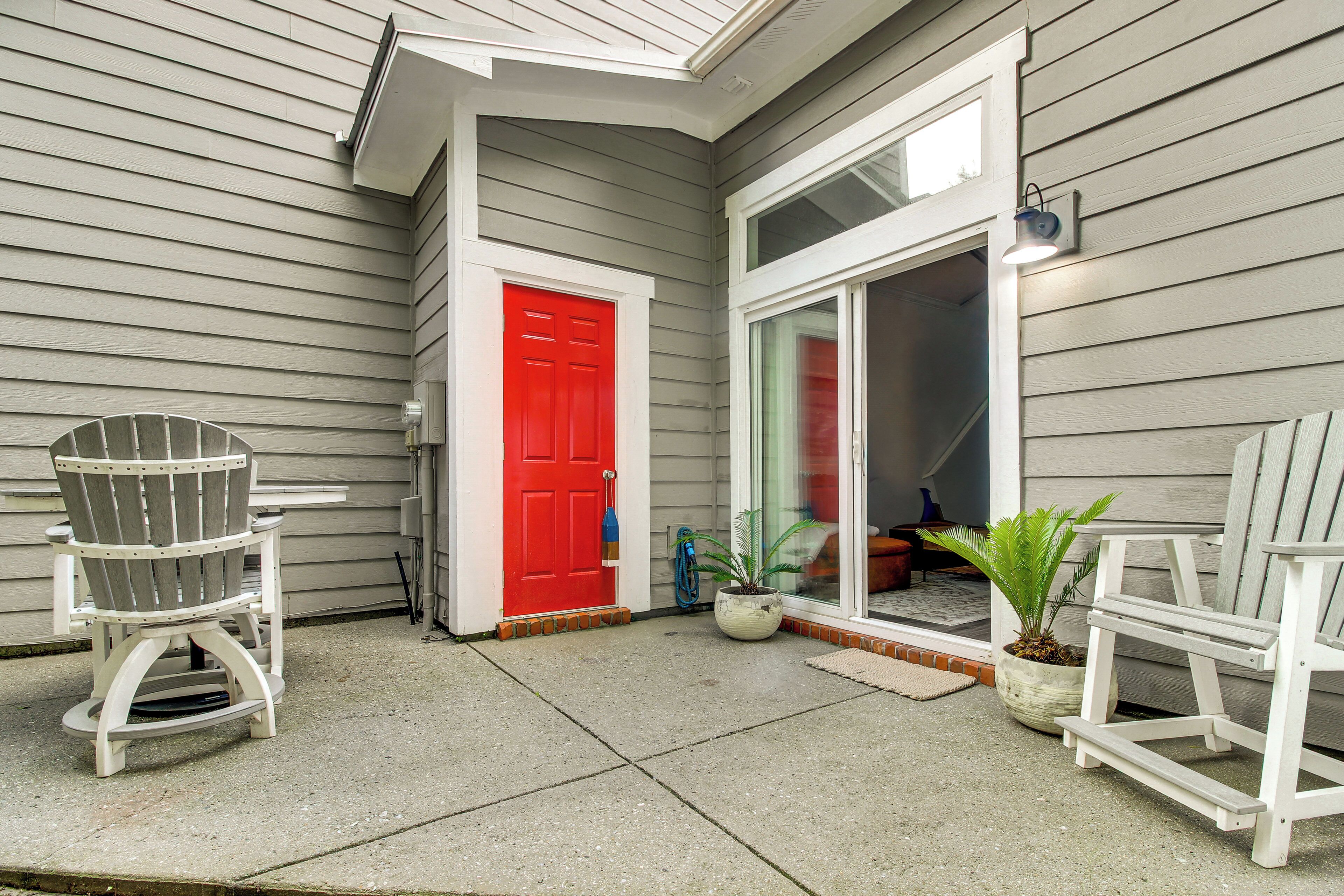 A covered porch with two Adirondack chairs, a red door, and a potted plant.