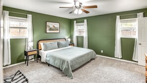 Un dormitorio con cama, mesitas de noche, ventilador de techo y ventana con cortinas.