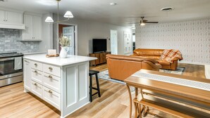 Una cocina moderna con armarios blancos, una isla central y un comedor con mesa y banco de madera.