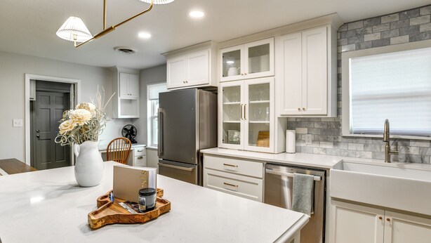 Una cocina moderna con muebles blancos, una isla central, electrodomésticos de acero inoxidable y un protector contra salpicaduras de piedra.