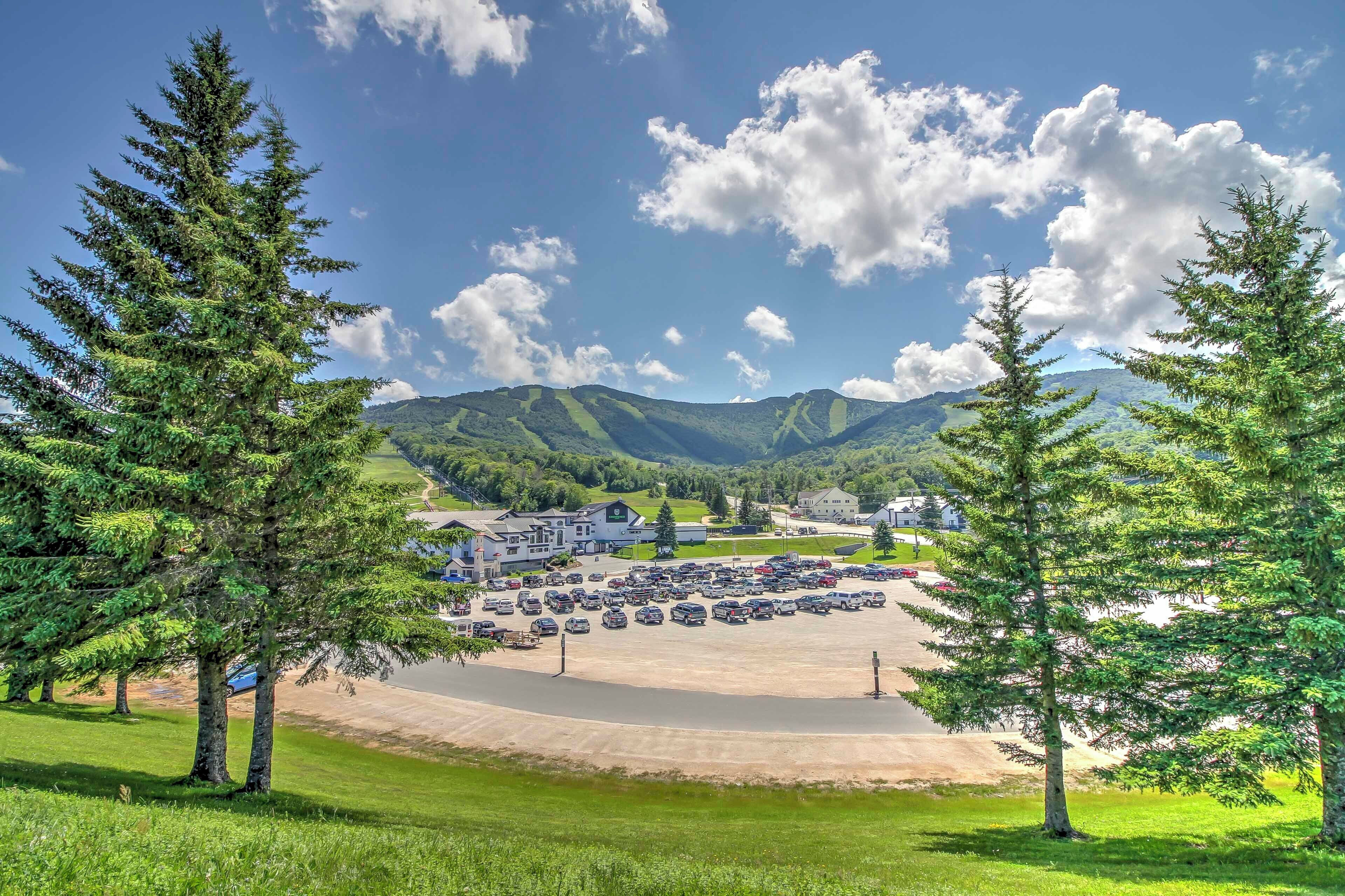A parking lot with several cars, surrounded by trees and buildings, with mountains in the background.