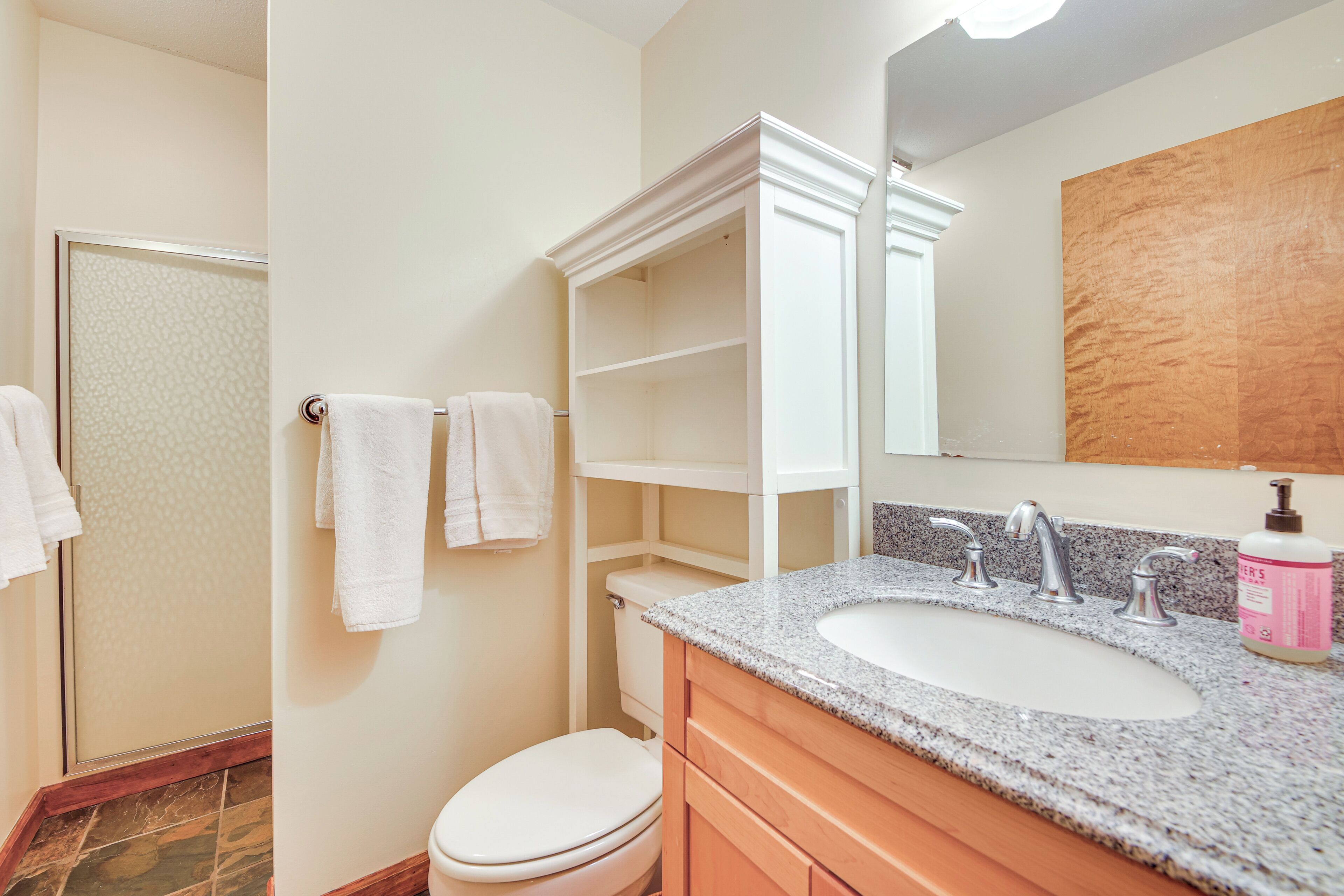 A bathroom with a white toilet, a granite sink, a wooden vanity, and a mirror above the sink.