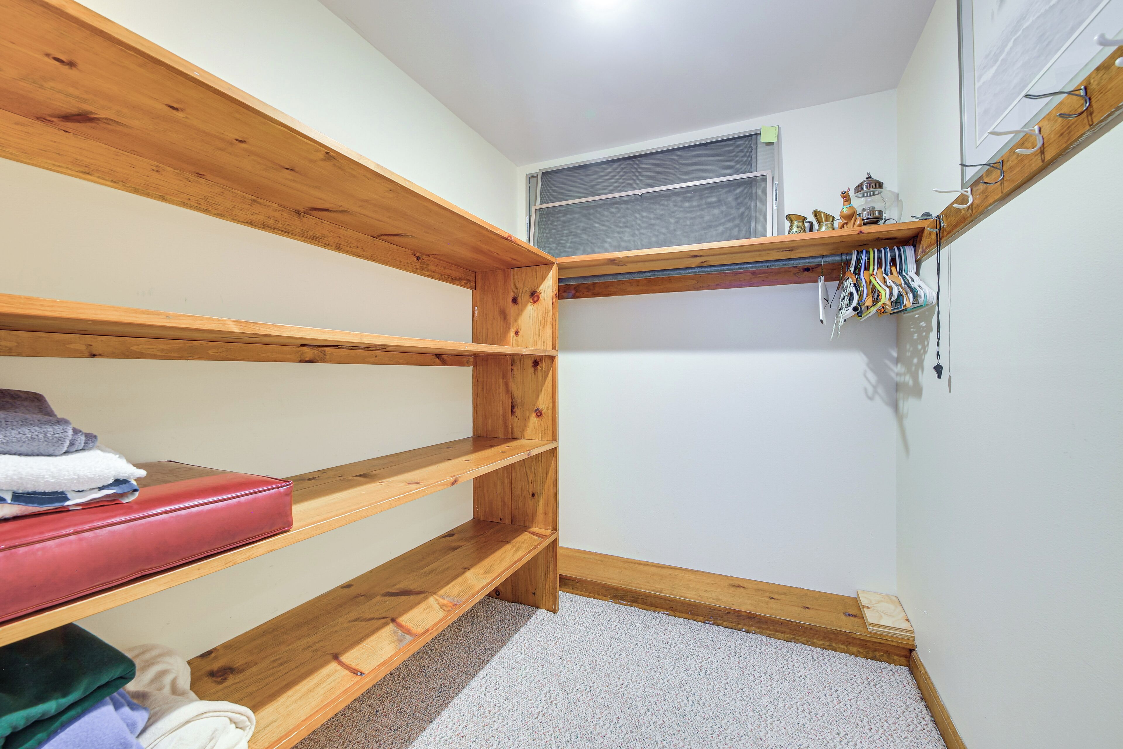 A small, neatly organized room with a wooden bunk bed, a small shelf with hanging items, and a window with an air conditioning unit.