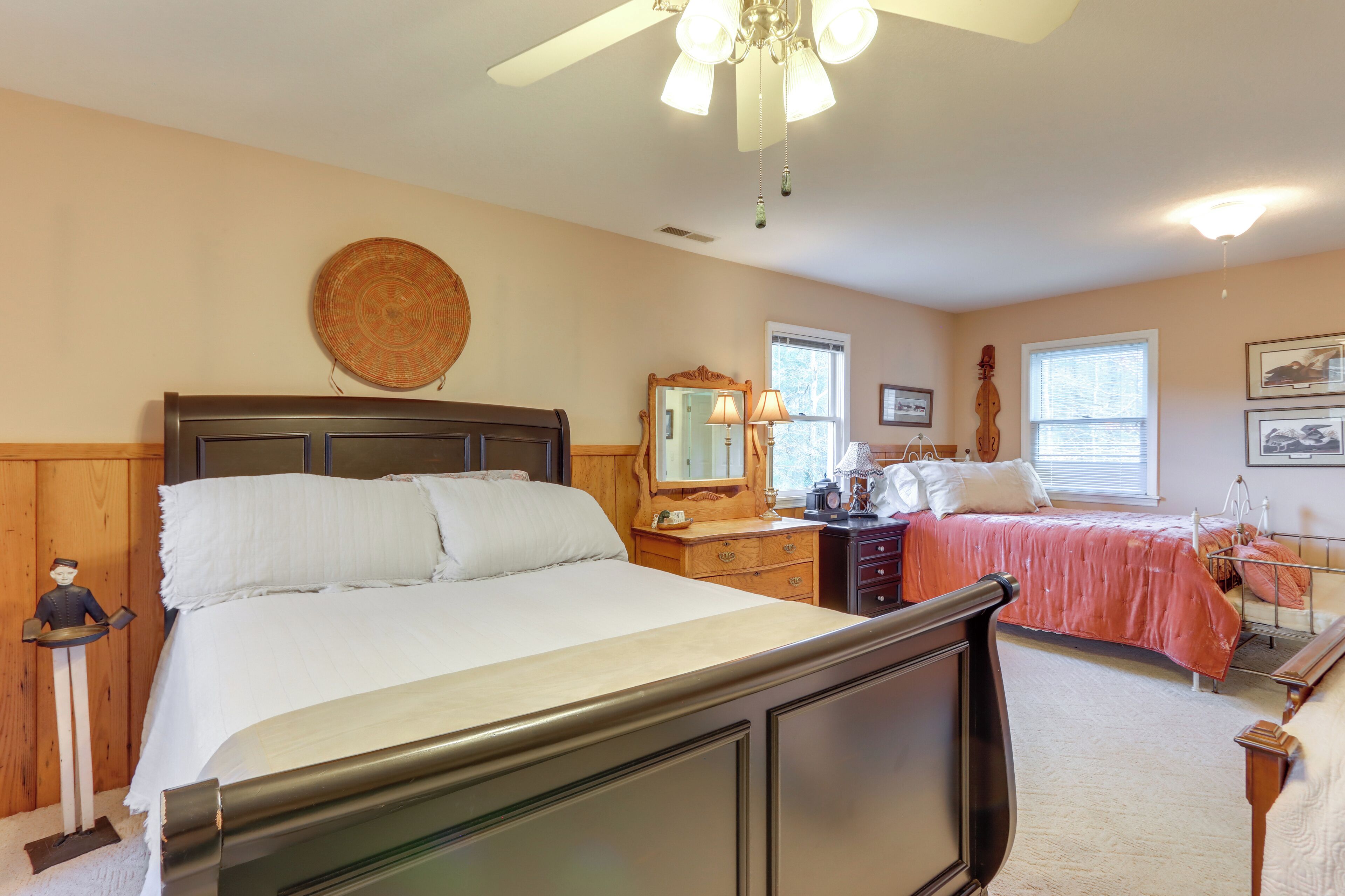 A bedroom with a large bed, a dresser, a nightstand, a mirror, and a ceiling fan.
