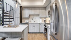 Una cocina moderna con una isla central, electrodomésticos de acero inoxidable y una escalera en espiral.