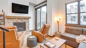 Una sala de estar moderna con chimenea, sillón de cuero, sofá y grandes ventanas con vistas a la ciudad.