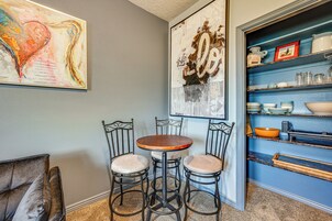 Un comedor con una mesa redonda y cuatro sillas, una estantería con diversos objetos, y dos grandes cuadros abstractos en la pared.