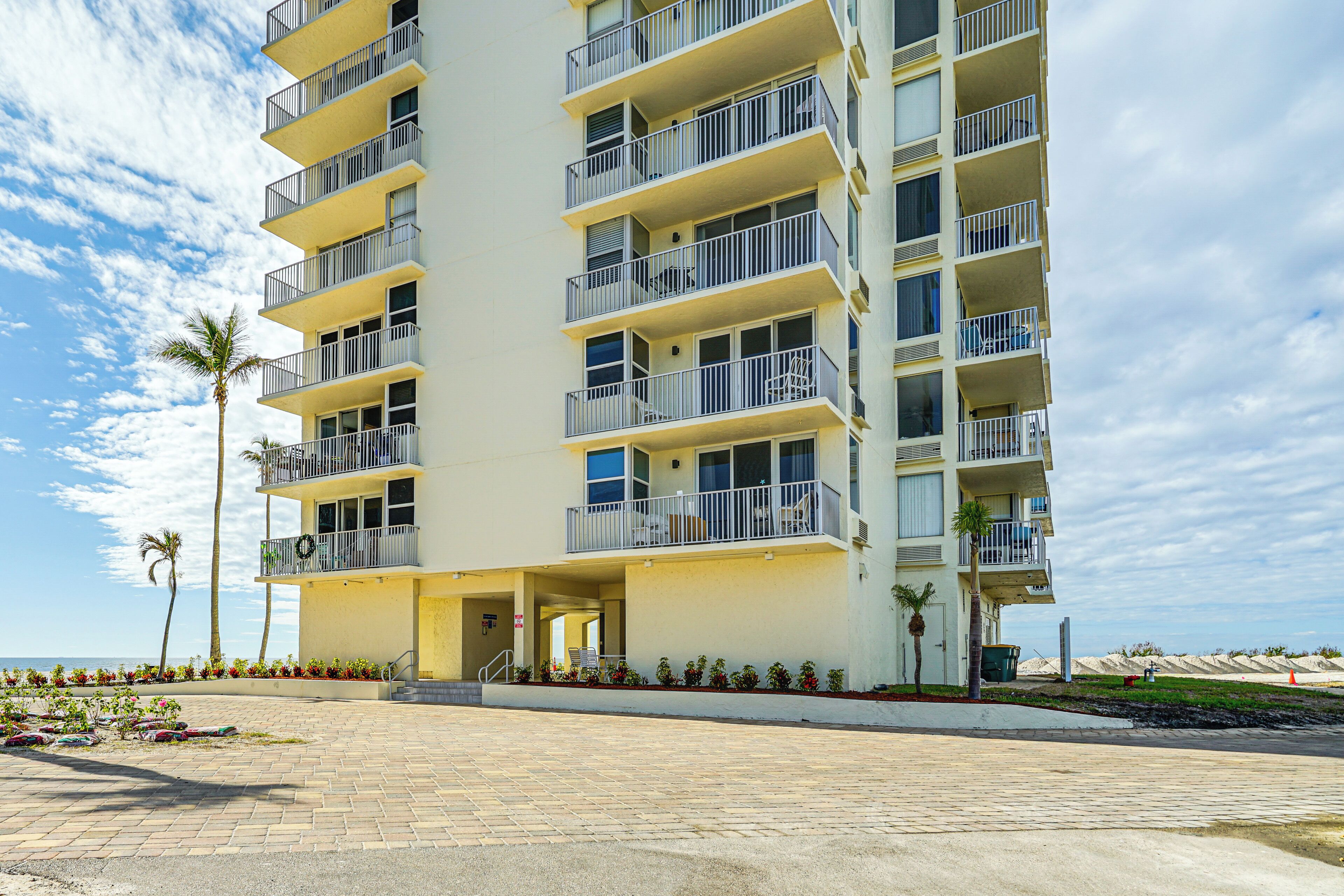 A multi-story hotel with balconies, a paved entrance, and a view of the beach.