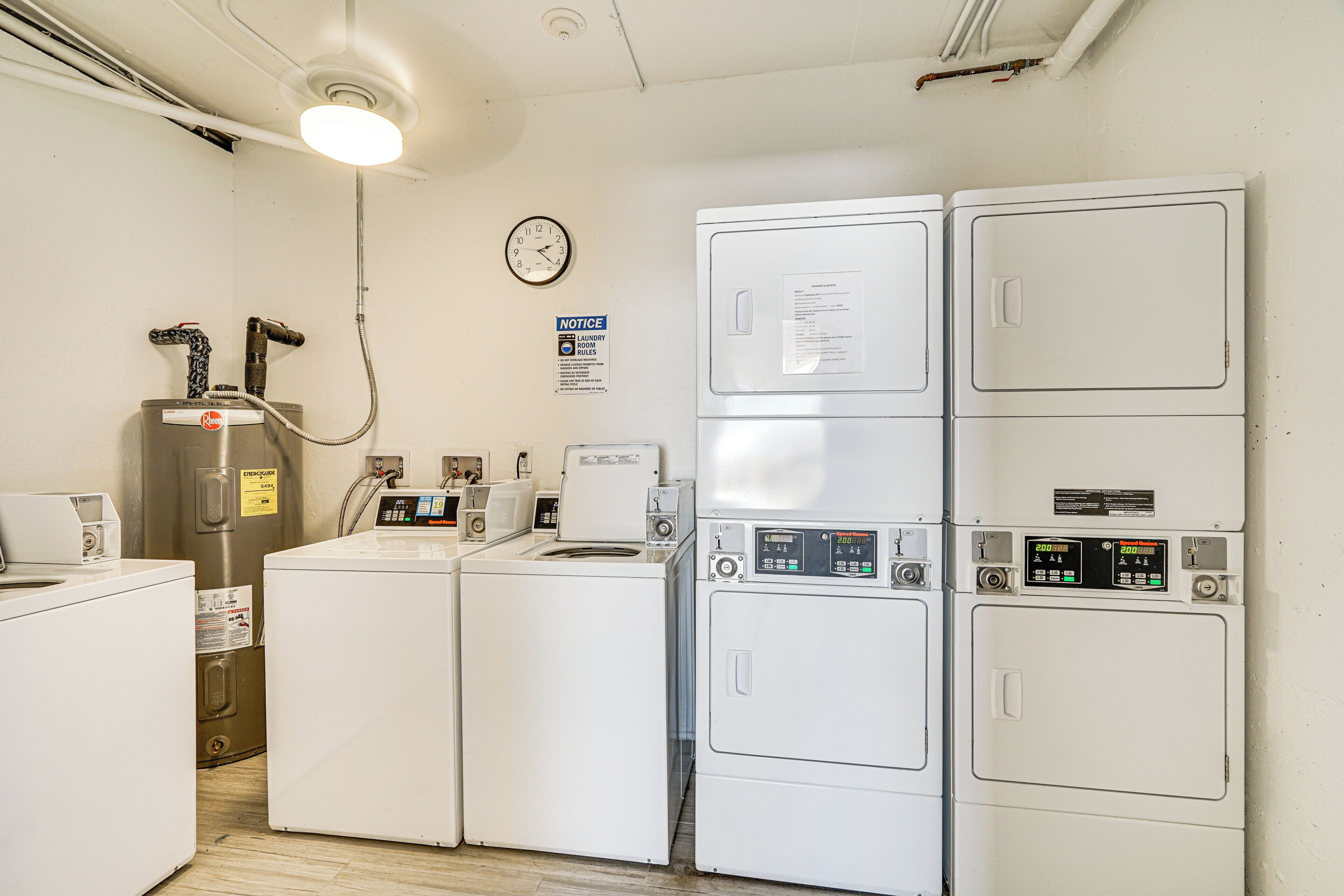 A laundry room with multiple washing machines, a dryer, and a water heater.