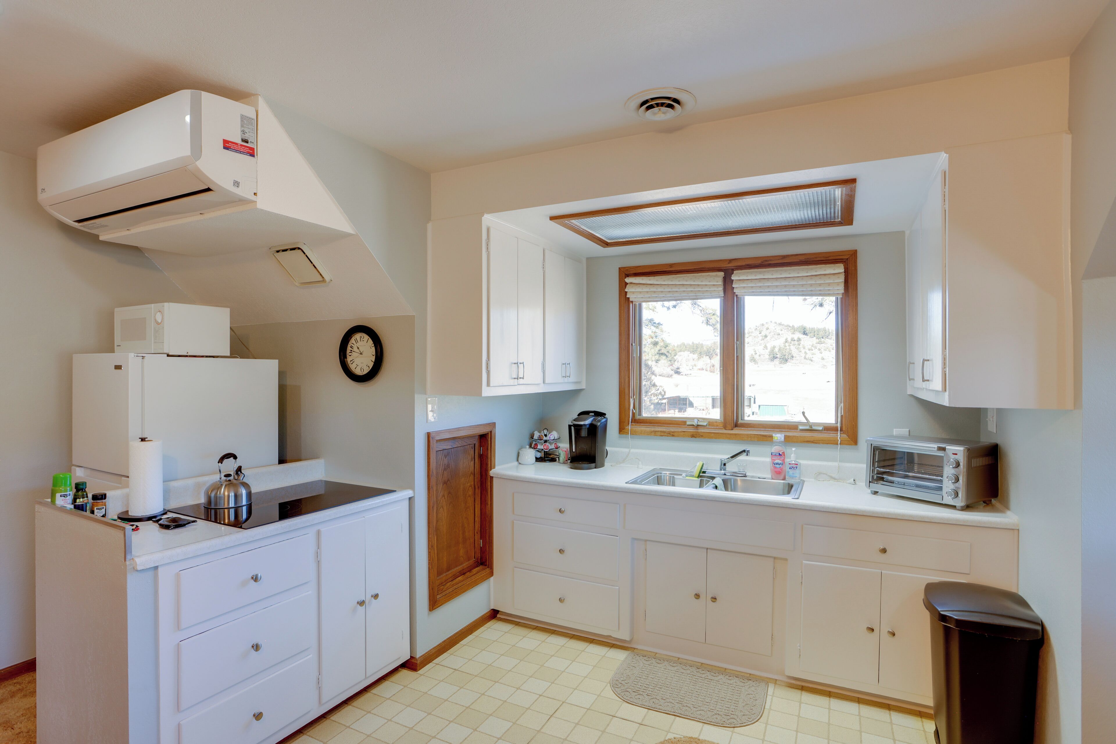 Cocina compacta con armarios blancos, microondas integrado, tostadora y ventana con vistas al exterior.