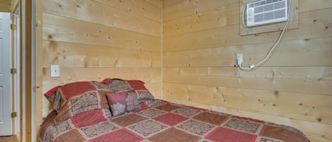Habitació amb panells de fusta, un llit, un aire condicionat fixat a la paret i una porta.