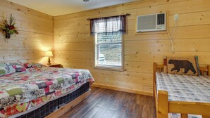 Habitación con paneles de madera, una cama, una mesita y ventana con vistas, además de un equipo de aire acondicionado.