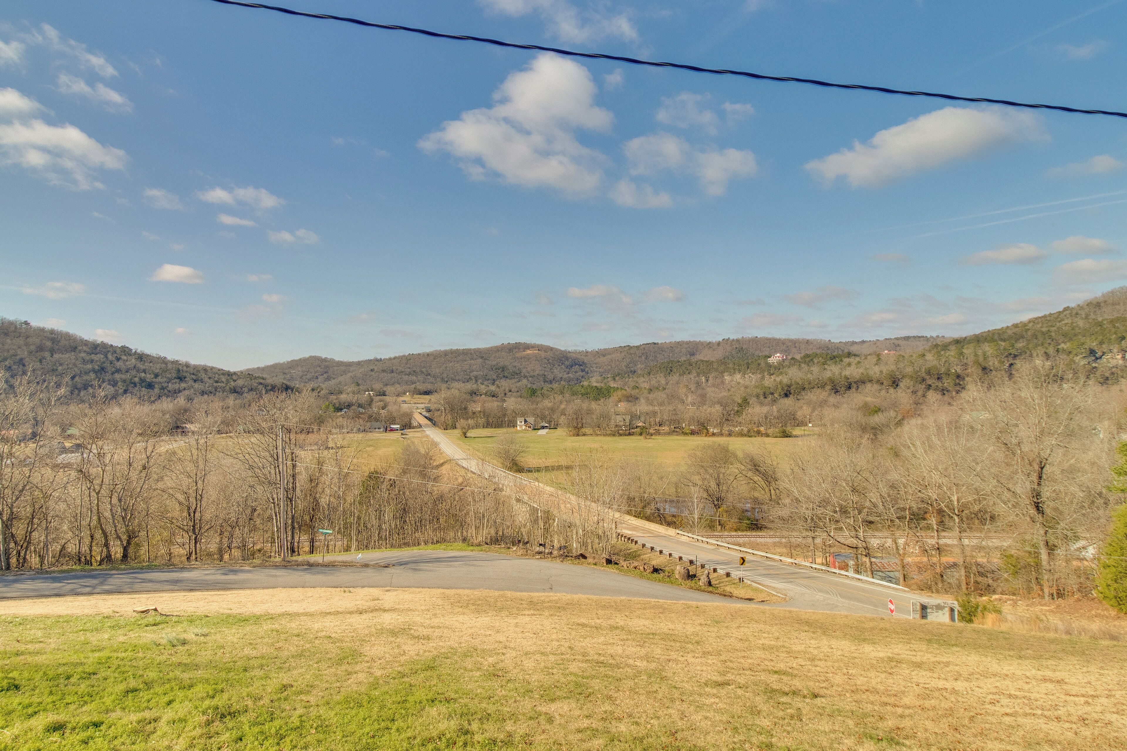 A rural landscape with a road curving through a valley, surrounded by hills and sparse trees.