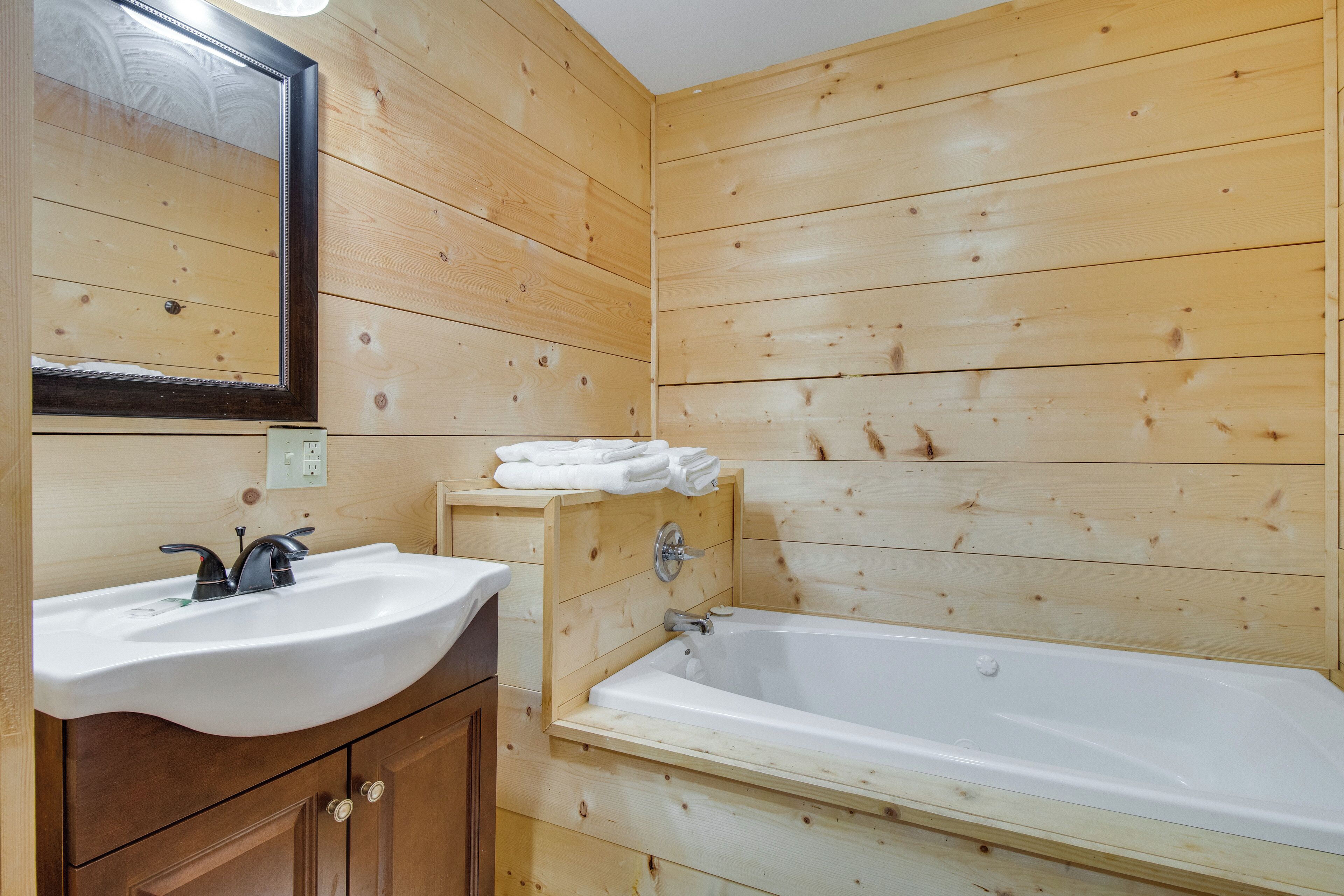 A wooden-paneled bathroom with a sink, mirror, and bathtub.