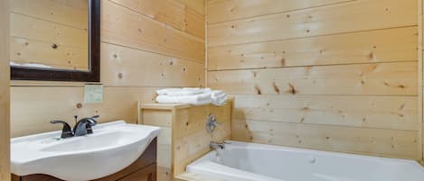 A wooden-paneled bathroom with a sink, mirror, and bathtub.