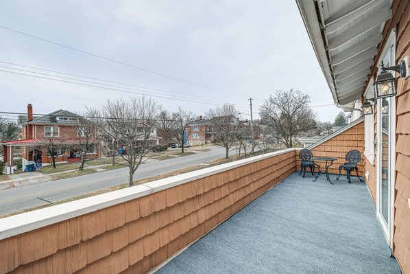 A balcony with a view of a street, a wooden wall, and two chairs.