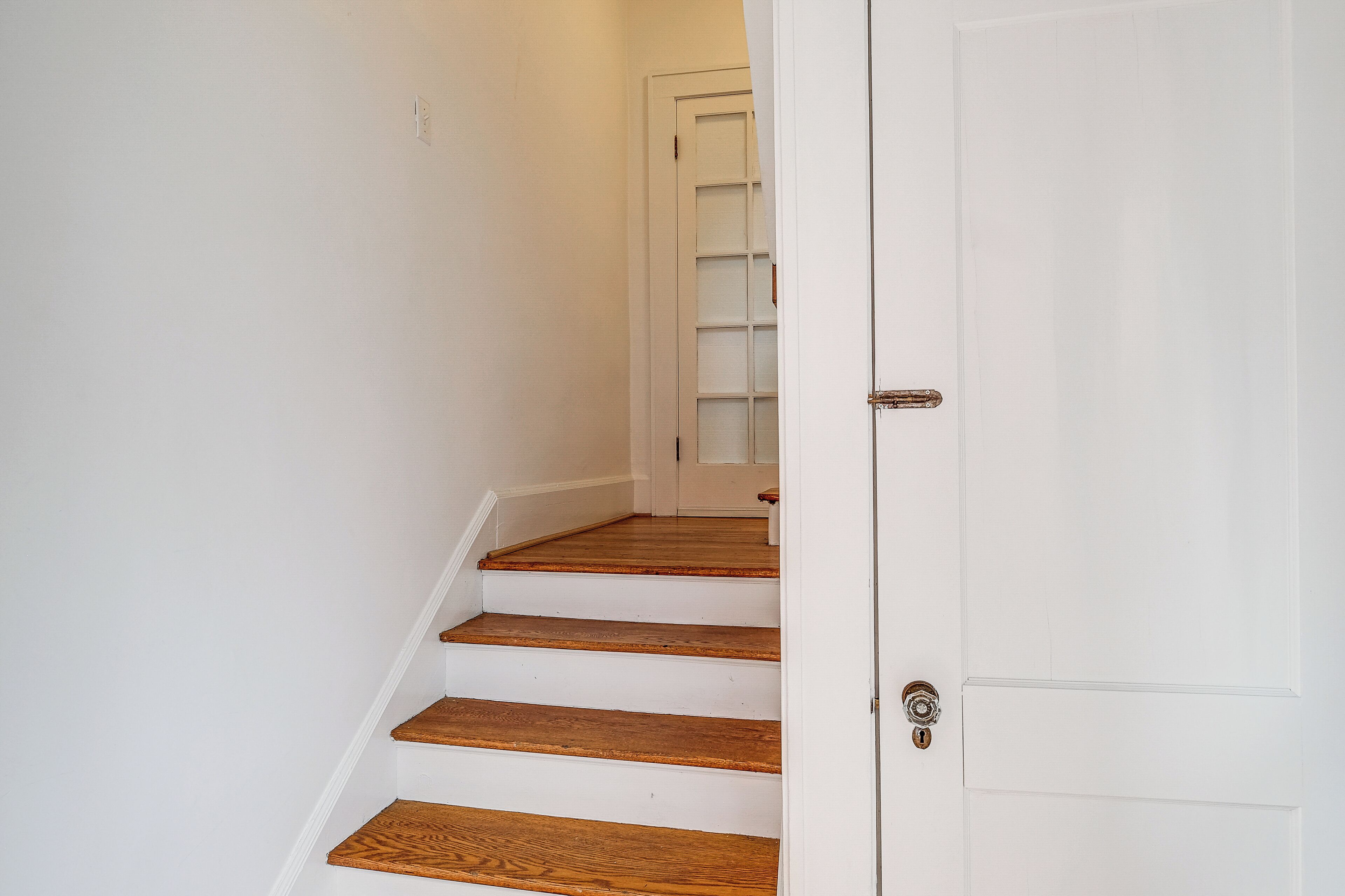 A staircase with wooden steps leading to a white door with a glass panel.