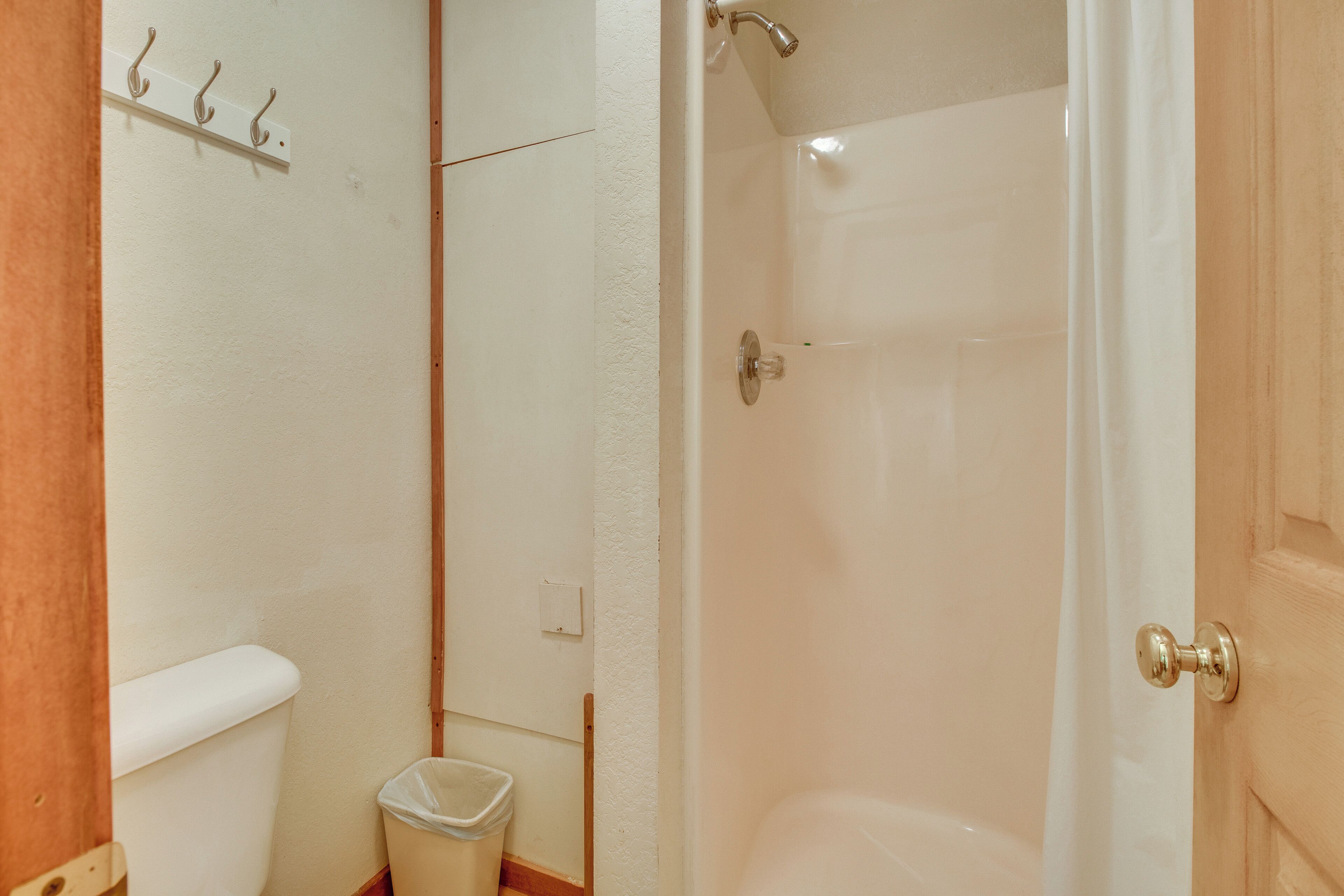 A bathroom with a toilet, a trash bin, and a shower stall.