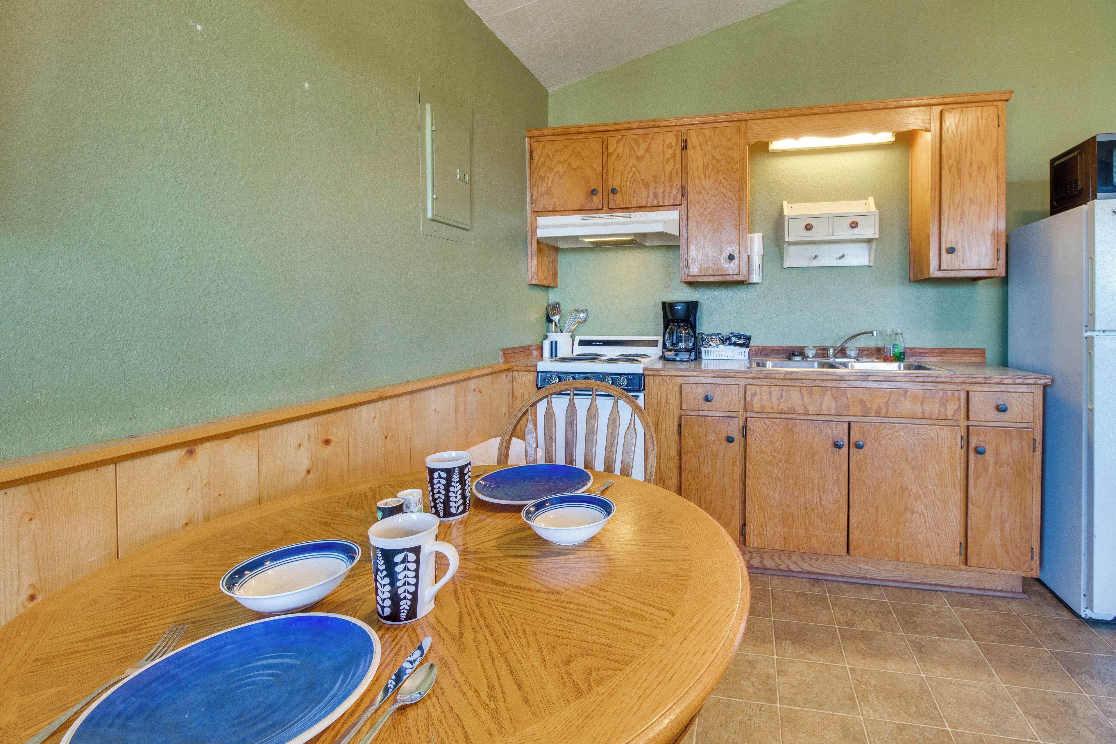 A kitchen with wooden cabinets, a dining table with blue plates and mugs, and a refrigerator.
