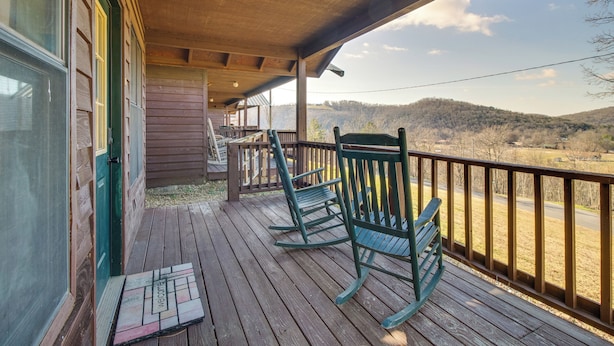 A wooden deck with rocking chairs and a view of a hilly landscape.