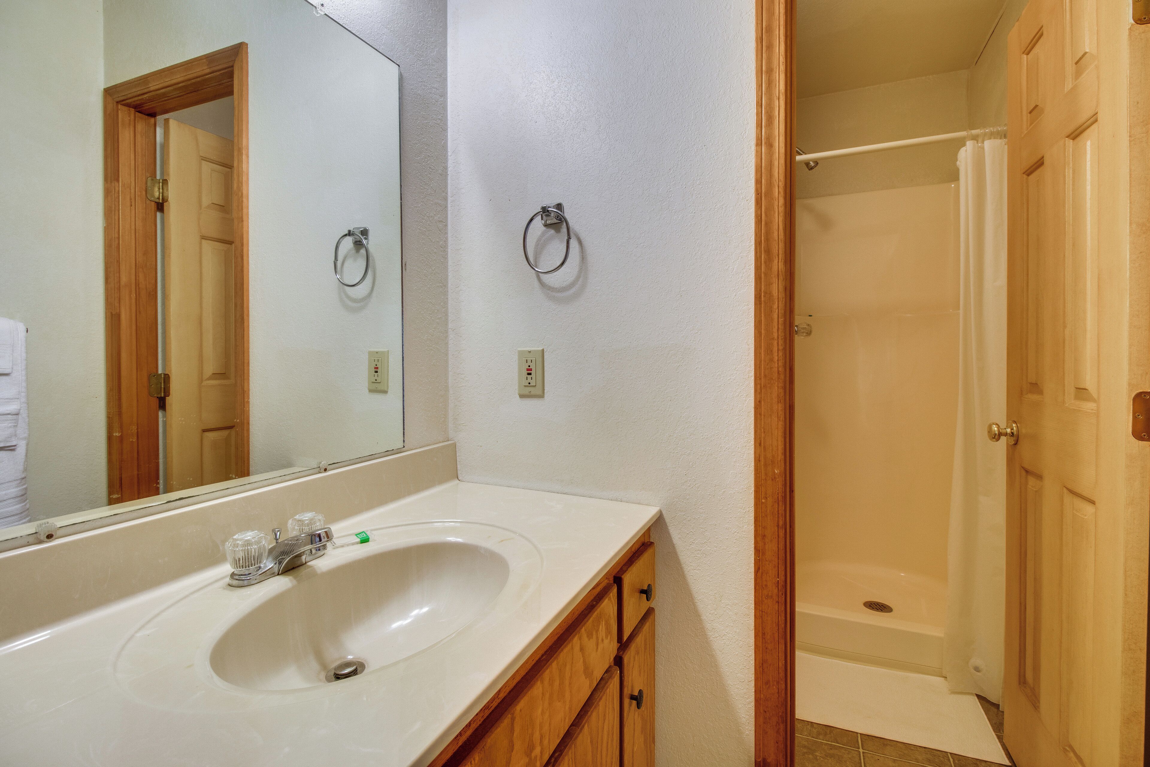 Ein Badezimmer mit Waschbecken, Spiegel, Dusche und Holzschränken.