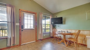 A room with a door, windows, a television, a table, and chairs.